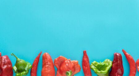 Row of peppers on blue background. Copy space. Top view.
