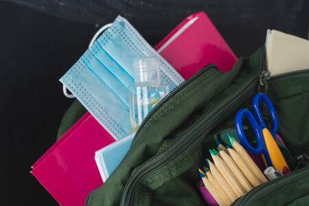 Backpack prepared with study supplies and mask for the return to school. Covid-19 concept.