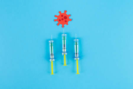 Three syringes stinging a red virus cut out of paper. Copy space. Concept Covid-19.の写真素材