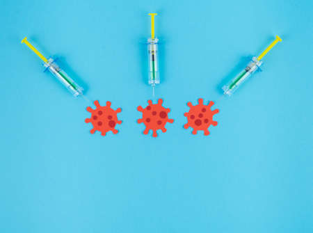 Three syringes stinging three red viruses cut out of paper. Copy space. Concept Covid-19.の写真素材