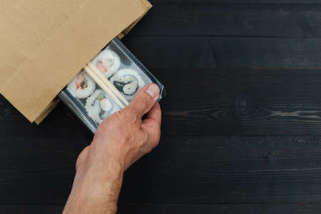Man's hand pulling sushi tray out of paper bag. Concept of packaged food. Copy space.の写真素材