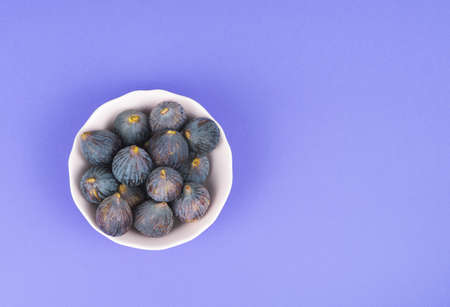 White bowl with whole ripe figs on a blue background Copy space.