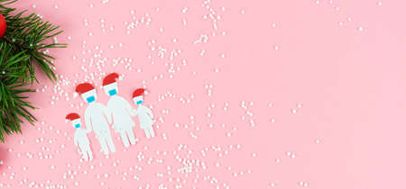 Paper cut family with mask and Christmas hat on a pink background with Christmas decoration. Copy space.の写真素材