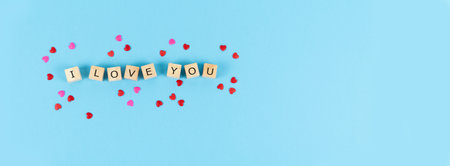 Valentine's Day. Letters I LOVE YOU on wooden cubes on blue background with hearts decorating. Copy space.の写真素材