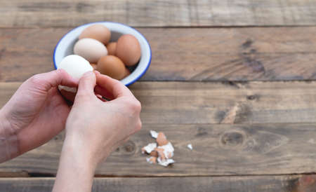 Hand peeling boiled eggs. Wooden background. Copy space. Bowl with eggs.の写真素材
