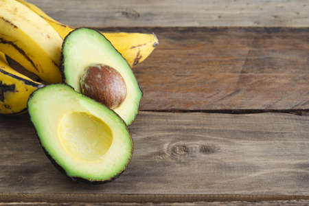 Avocado cut in half and banana on wooden background. Copy space.の写真素材