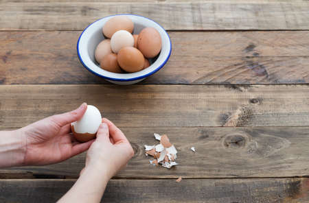 Hand peeling boiled eggs. Wooden background. Copy space. Bowl with eggs.の写真素材