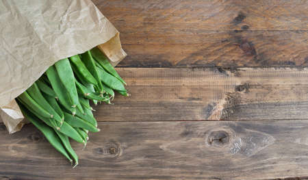 Green beans in paper bag on wooden background. Vegetables concept.の写真素材