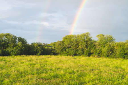 Landscape of meadows and trees with double rainbow with sky with clouds.の写真素材