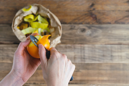 Peeling orange and bag of peels for compost. Copy space. Rustic wood background.