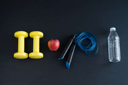 Dumbbells and jump rope on black background for home exercise. Copy space.