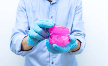 Dentist in gloves and blue shirt showing dental splint in protective box. Copy space.