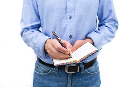 Man in blue shirt and blue jeans writing on a pad of paper with a pen. Copy space.