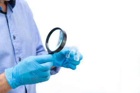 Dentist examining with magnifying glass a transparent dental splint on white background. Copy space.の写真素材