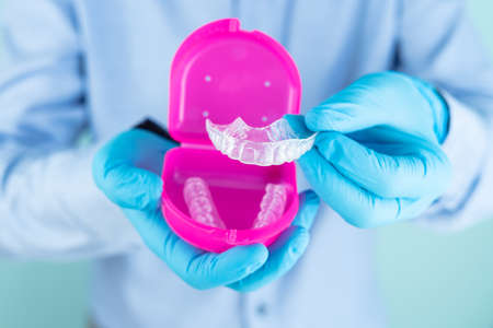 Doctor in blue shirt and gloves showing a dental splint in pink box.の写真素材