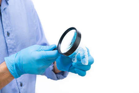 Dentist in blue shirt and white background examining a dental splint with magnifying glass. Copy space.の写真素材