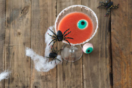 Red colored cocktail for Halloween day with spider and eye on rustic wooden background. Copy space.の写真素材