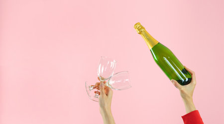 Hands with crystal glasses and champagne bottle. Pink background. Copy space.の写真素材