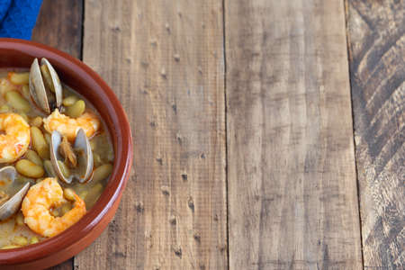 Fabas verdinas with prawns and clams in an earthenware casserole on a wooden base. Copy space. super viewの写真素材