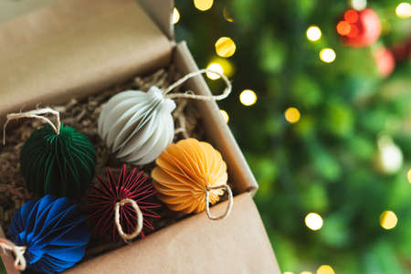 Colored balls made of paper for Christmas ornament in box with tree and lights in the background. Copy space.の写真素材