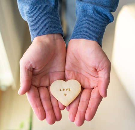 Man hands offering heart-shaped cookie. Letters LOVE. Valentine Day concept.の写真素材