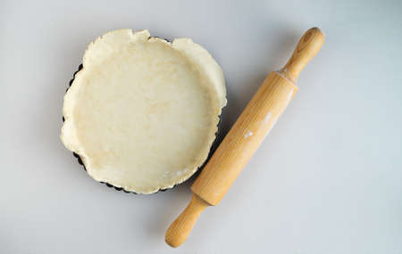 Bakery mold with dough base and wooden rolling pin on white background. Top view.の写真素材