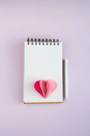 Blank notebook with pen and paper heart on lilac background. Valentine's Day and Mother's Day. Copy space. Vertical photos.の写真素材