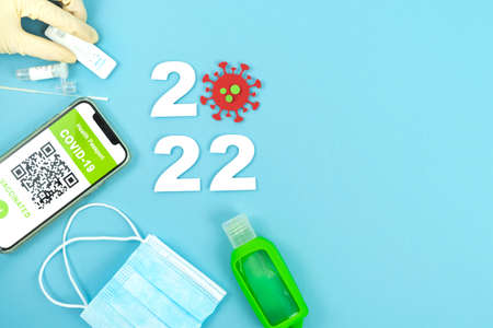 Year 2022. Coronavirus pandemic. Mobile with covid certificate, mask and antigen test on blue...