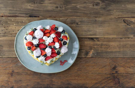 Heart-shaped cake decorated with red fruits and meringue. Rustic wooden background. Valentine's Day. Copy space.の写真素材