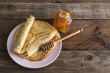Crepes with honey on wooden background on pink plate with honey spoon. Copy space.
