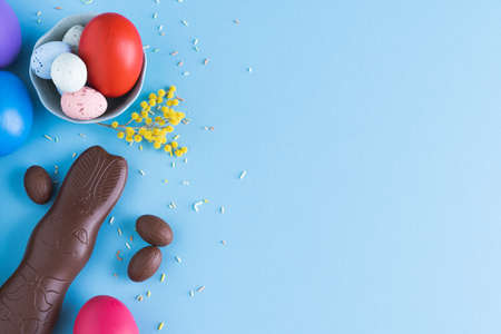 Easter eggs and chocolate bunny on blue background with yellow flower decorations. Top view. Copy space.の写真素材