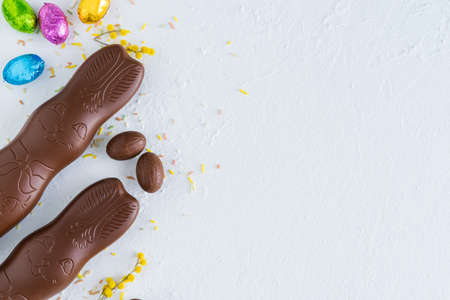 Easter eggs and chocolate bunny on white background with yellow flower decorations. Top view. Copyspace.の写真素材