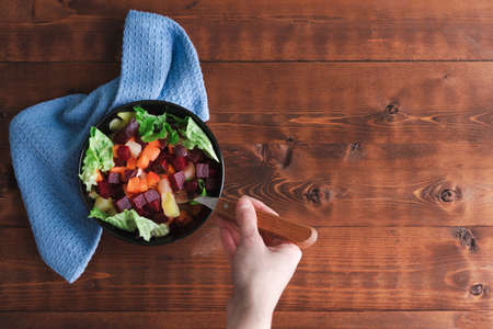 Woman hand eating salad of beet, carrot and lettuce in bowl on wooden background. Copyspace. Top view.の写真素材