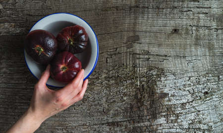 Hand clutching a blue sea tomato from a white plate on old wood background. Copyspace. Top view.