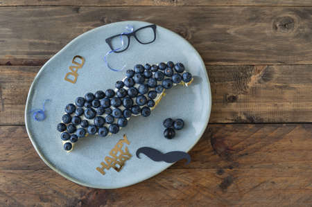Mustache shaped cake with blueberries and decoration on wooden background. Copyspace. Father's day. Masculine concept.の写真素材