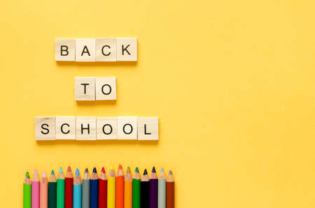 Back to class. Colored pencils and letters in wooden cubes BACK TO SCHOOL on yellow background. Copy space. Topview.の写真素材
