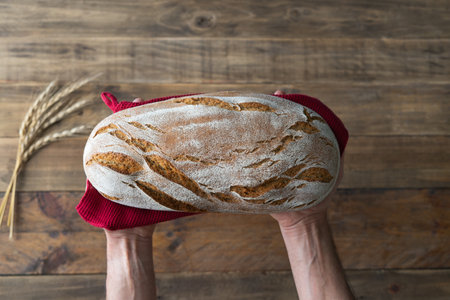 Hands showing a piece of rustic bread on wooden background with red napkin ornament. Copyspace. top view.の写真素材