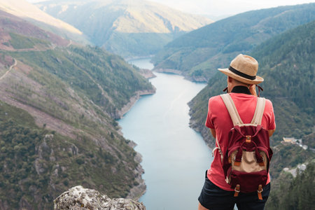 Man with hat and backpack taking photo of mountain landscape with river on sunny day. Copyspace.の写真素材