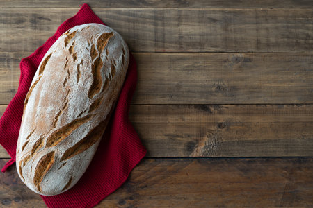 Piece of rustic bread on wooden background with red napkin ornament. Copyspace. top view.の写真素材