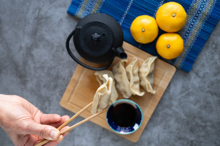 Asian food. Hand picking up food with chopsticks. Dim sum with soy sauce on bamboo board decorated with oranges and teapot. Copyspace. top view.の写真素材