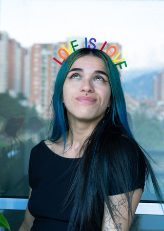 Young woman with blue hair looking upwards with gay themed headband. LOVE IS LOVE. Vertical photos. Copyspace.の写真素材