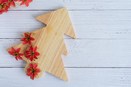 Wooden Christmas tree with red flower decoration on white wooden boards with space for text.の写真素材
