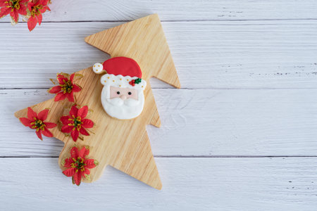 Wooden Christmas tree with red flowers decoration and Santa's face biscuit on white wooden background. Top view.の写真素材