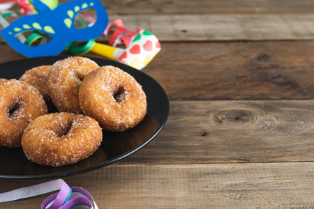 Sweet donuts carnival dessert on black plate on wooden background with typical carnival decorations. Copy space.の写真素材