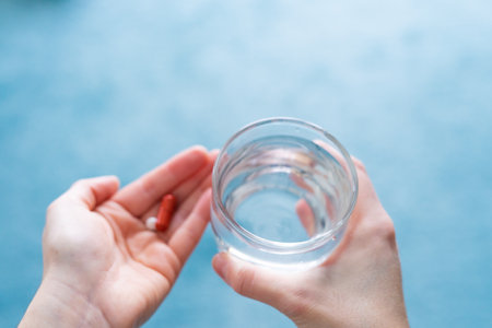 Woman's hands about to take a pill, glass of water and copy space.の写真素材