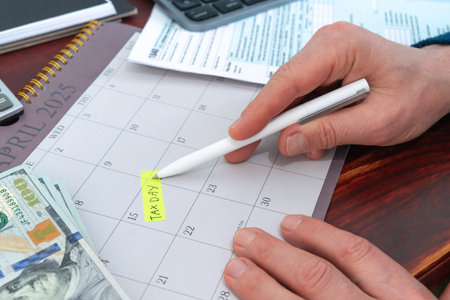 Hand pointing to the day of paying taxes in the United States, next to your dollars, calculator and a tax form.の写真素材
