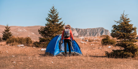 A man with a tent enjoys a sunny day whileusing a smartphone and camping in the mountainsの写真素材