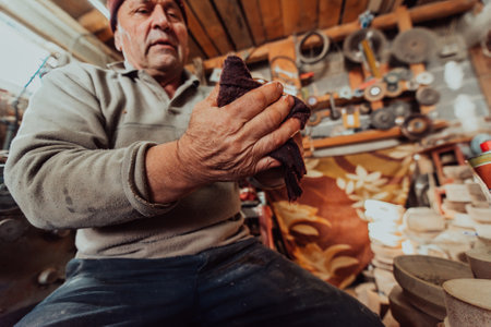 A senior man sitstingin the workshop and smearsing wooden utensils with linseed oilの写真素材