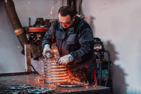 Locksmith in special clothes and goggles works in production. Metal processing with angle grinder. Sparks in metalworking.の写真素材