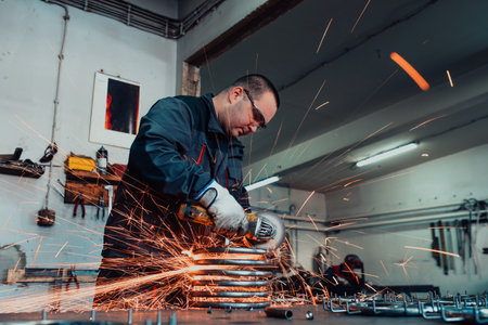 Locksmith in special clothes and goggles works in production. Metal processing with angle grinder....